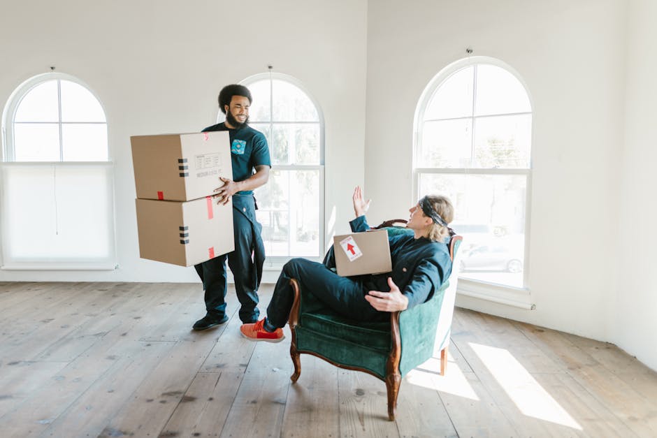 Three individuals standing outside a property in front of a large window with wooden framing, smiling and taking a selfie together during a house moving process. Each person is holding a cardboard box